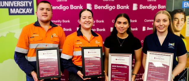 A group of scholarship recipients standing in front of a Community Bank Sarina branded pull up banner holding certificates. 