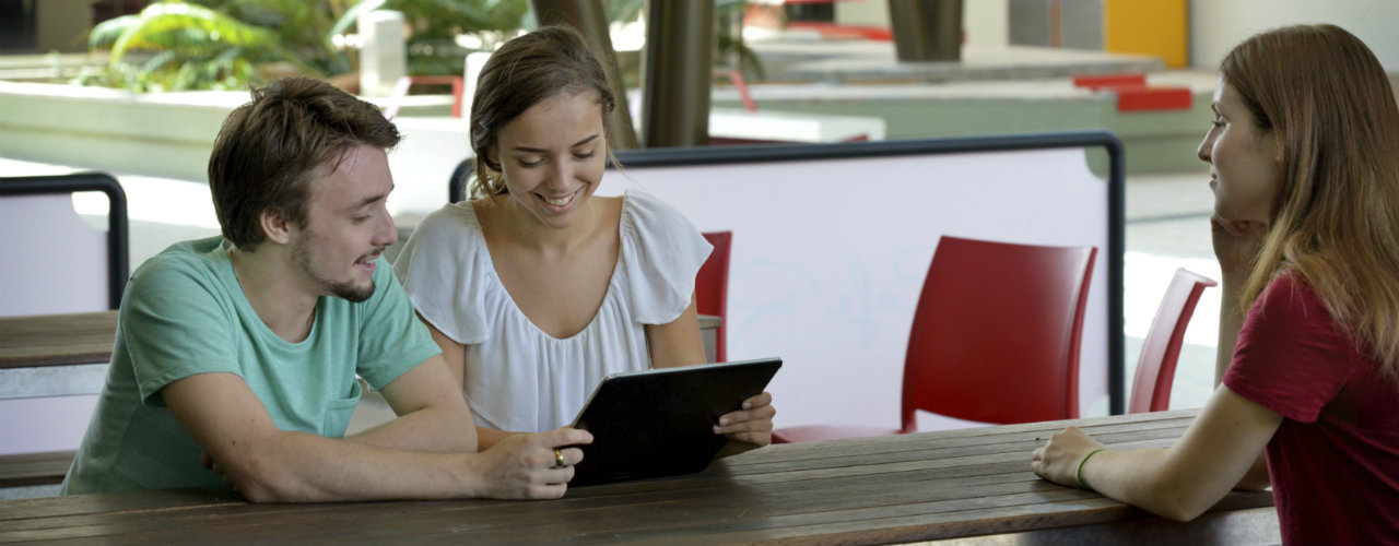 Three students sitting at table looking at iPad.